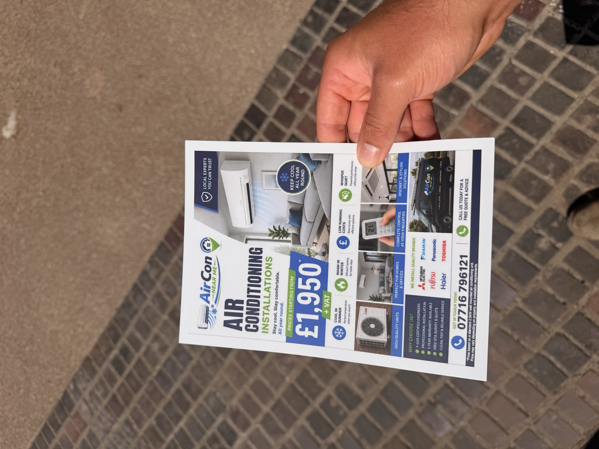 Printed A5 marketing flyer held against a paved background