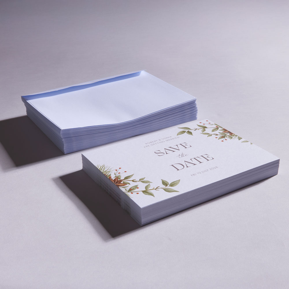 Stack of printed wedding invitations with envelopes and greenery design